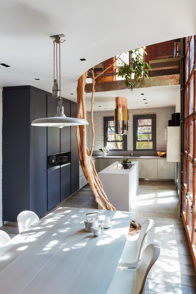 Trendy u-shaped light wood floor open concept kitchen photo in London with flat-panel cabinets, blue cabinets, white backsplash, brick backsplash, black appliances and an island
