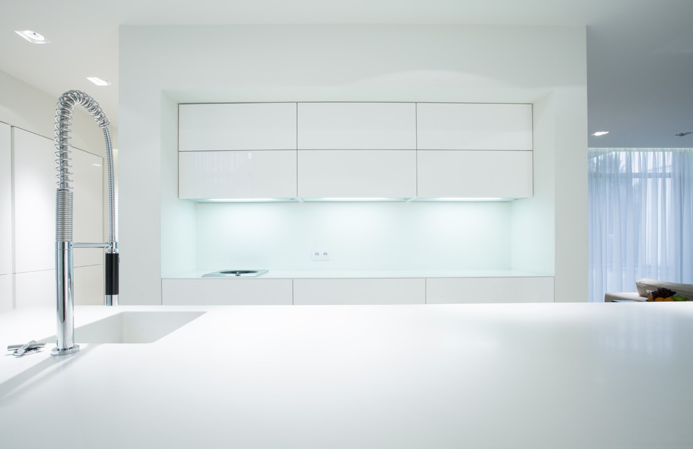 Modelo de cocina comedor minimalista con puertas de armario blancas, salpicadero blanco, una isla y encimeras blancas