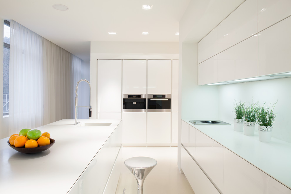 Imagen de cocina comedor moderna con puertas de armario blancas, salpicadero blanco, una isla y encimeras blancas