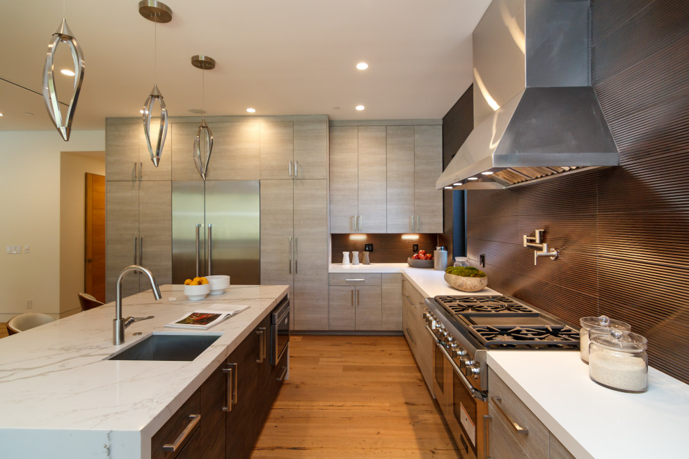 Foto på ett mycket stort funkis vit l-kök, med en undermonterad diskho, släta luckor, grå skåp, svart stänkskydd, rostfria vitvaror, mellanmörkt trägolv, en köksö och brunt golv