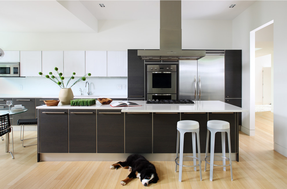 Cette image montre une cuisine américaine parallèle design avec un placard à porte plane, des portes de placard noires, une crédence blanche et un électroménager en acier inoxydable.