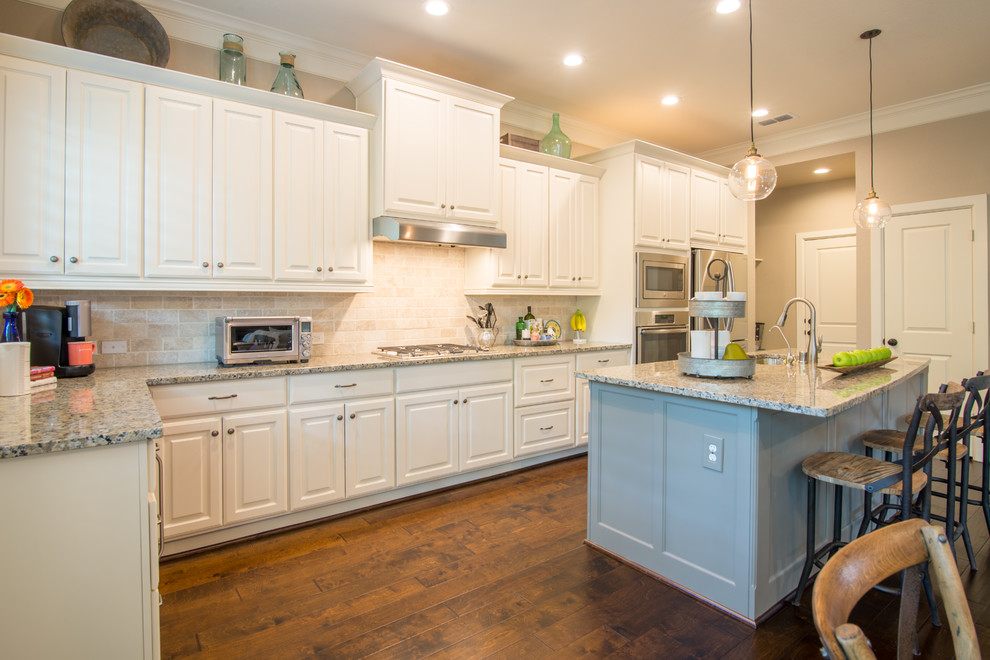Inspiration for a small transitional l-shaped medium tone wood floor eat-in kitchen remodel in Houston with a double-bowl sink, raised-panel cabinets, white cabinets, granite countertops, beige backsplash, stone tile backsplash, stainless steel appliances and an island