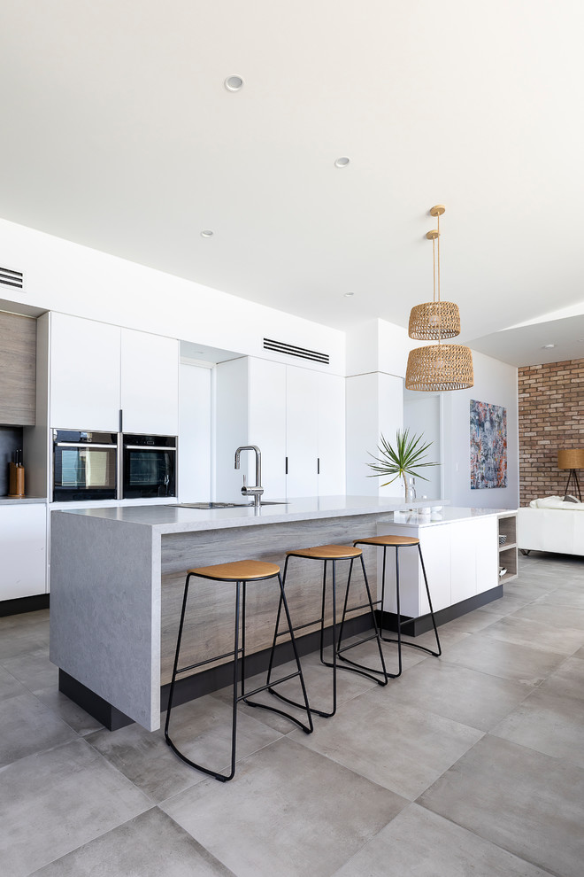 This is an example of a large contemporary l-shaped open plan kitchen in Brisbane with a single-bowl sink, flat-panel cabinets, white cabinets, engineered stone countertops, grey splashback, ceramic splashback, black appliances, cement flooring, an island, grey floors and grey worktops.