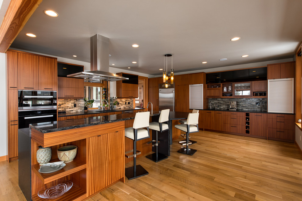Moderne Küche in L-Form mit flächenbündigen Schrankfronten, dunklen Holzschränken, Küchenrückwand in Grau, Küchengeräten aus Edelstahl, braunem Holzboden, Kücheninsel und braunem Boden in Sonstige