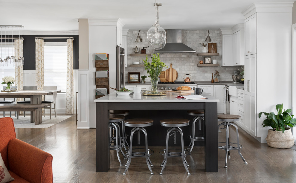 Example of a mid-sized transitional u-shaped medium tone wood floor and brown floor open concept kitchen design in Chicago with a farmhouse sink, shaker cabinets, white cabinets, quartz countertops, marble backsplash, stainless steel appliances, an island, gray countertops and gray backsplash