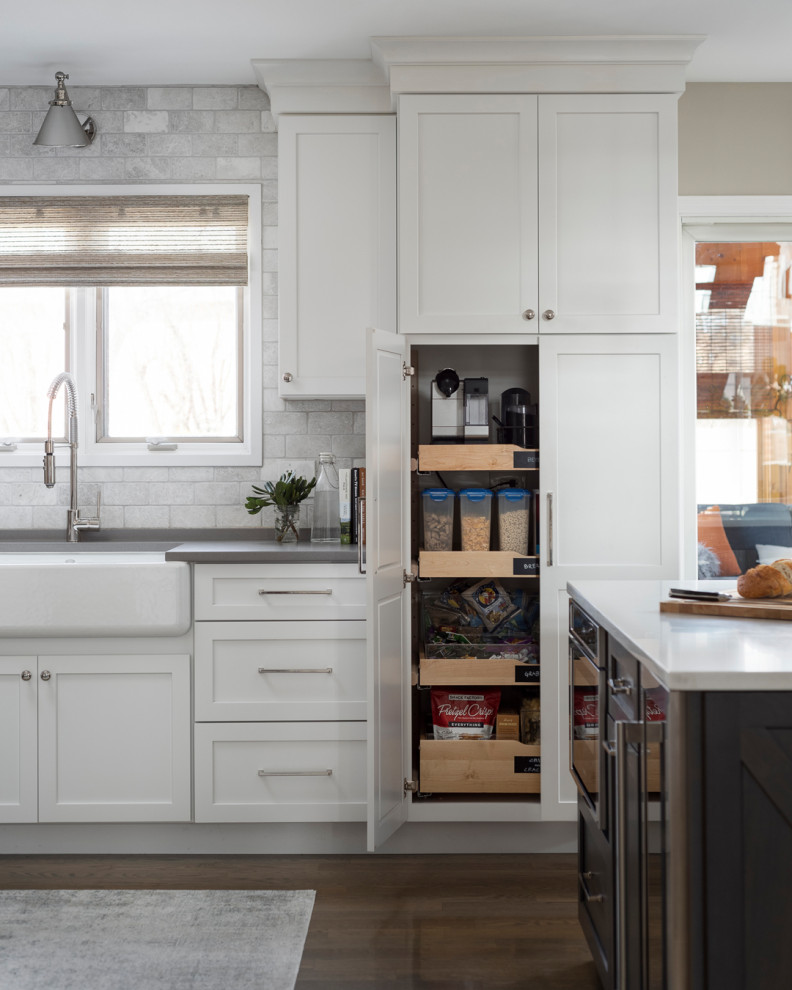 Klassisk inredning av ett mellanstort grå grått kök, med en rustik diskho, skåp i shakerstil, vita skåp, bänkskiva i kvarts, vitt stänkskydd, stänkskydd i marmor, rostfria vitvaror, mellanmörkt trägolv, en köksö och grått golv