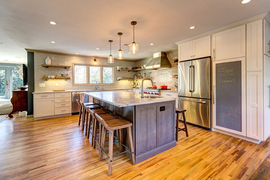 Large trendy l-shaped medium tone wood floor and brown floor open concept kitchen photo in Boston with an undermount sink, shaker cabinets, white cabinets, granite countertops, white backsplash, ceramic backsplash, stainless steel appliances and an island