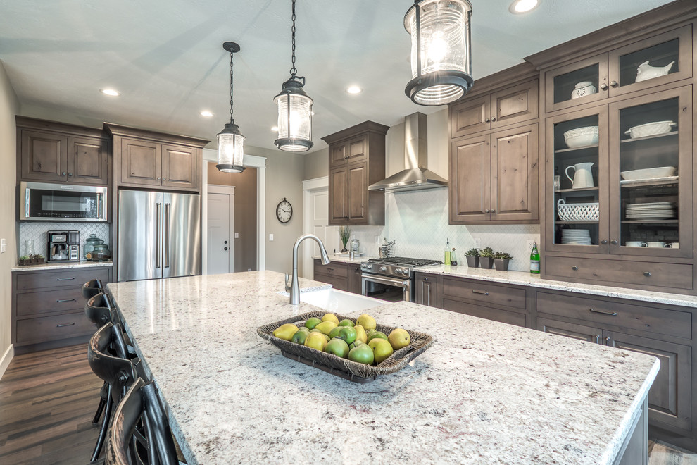 Inspiration for a mid-sized rustic single-wall medium tone wood floor open concept kitchen remodel in Other with a farmhouse sink, raised-panel cabinets, gray cabinets, granite countertops, white backsplash, ceramic backsplash, stainless steel appliances and an island