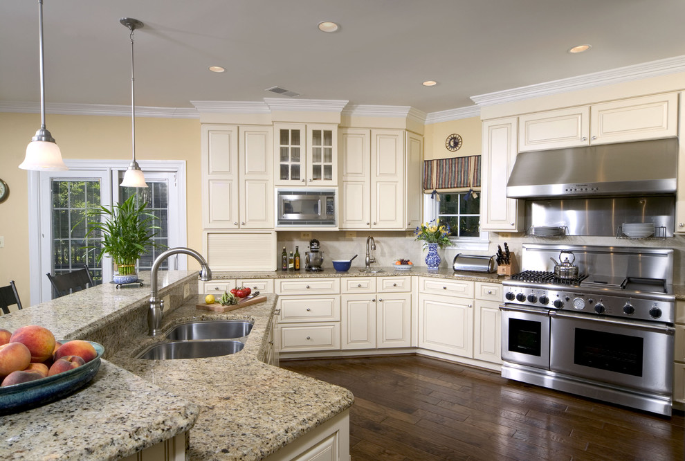 Klassisk inredning av ett kök, med en dubbel diskho, rostfria vitvaror, granitbänkskiva, luckor med upphöjd panel och beige skåp