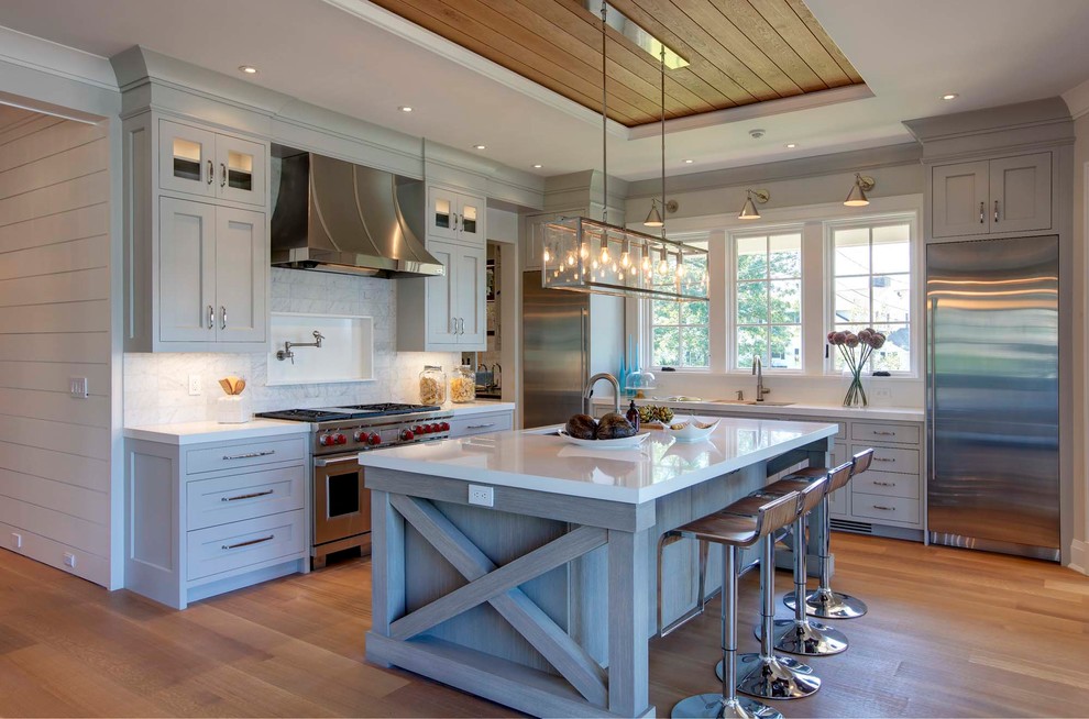 Photo of a coastal kitchen in New York with a submerged sink, shaker cabinets, grey cabinets, grey splashback, stainless steel appliances, light hardwood flooring and an island.