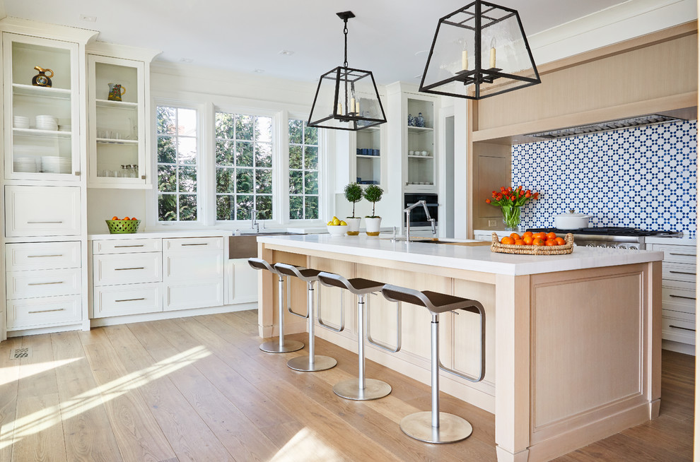 Inspiration for a beach style kitchen in New York with a submerged sink, white cabinets, multi-coloured splashback, stainless steel appliances, light hardwood flooring, an island, beige floors, white worktops and recessed-panel cabinets.