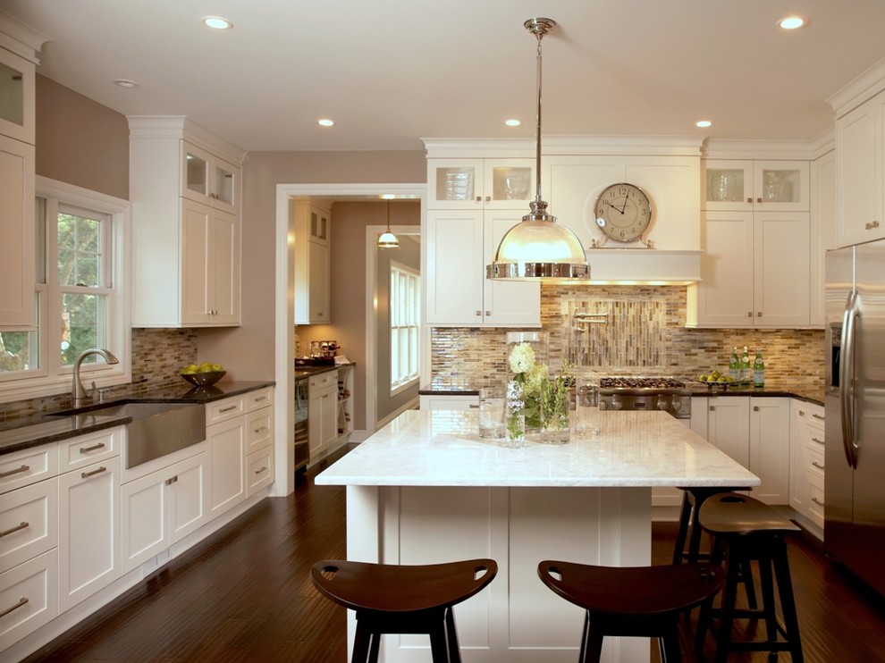 Klassisk inredning av ett kök, med en rustik diskho, luckor med infälld panel, vita skåp, rostfria vitvaror, mörkt trägolv och en köksö