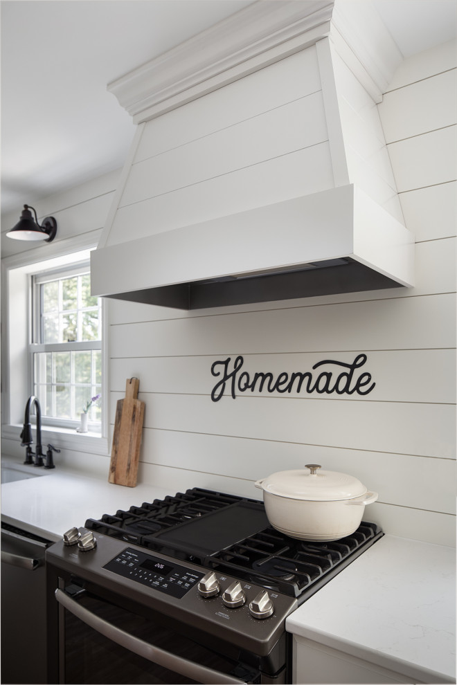 Photo of a medium sized rural kitchen/diner in Other with a belfast sink, shaker cabinets, white cabinets, engineered stone countertops, white splashback, wood splashback, stainless steel appliances, vinyl flooring, an island, brown floors and white worktops.