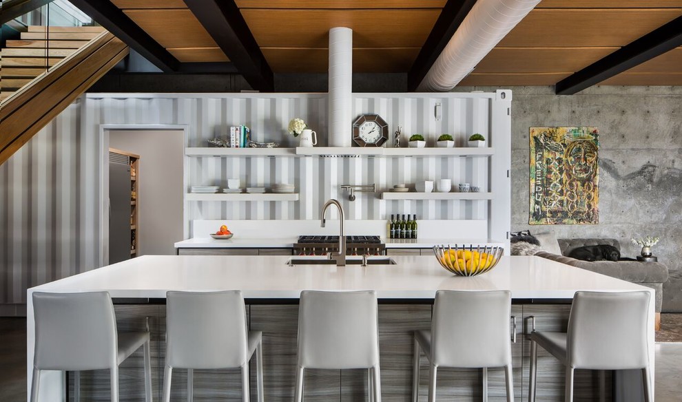 На фото: параллельная кухня-гостиная в стиле лофт с врезной мойкой, плоскими фасадами, серыми фасадами, техникой из нержавеющей стали, бетонным полом, островом, серым полом и белой столешницей с