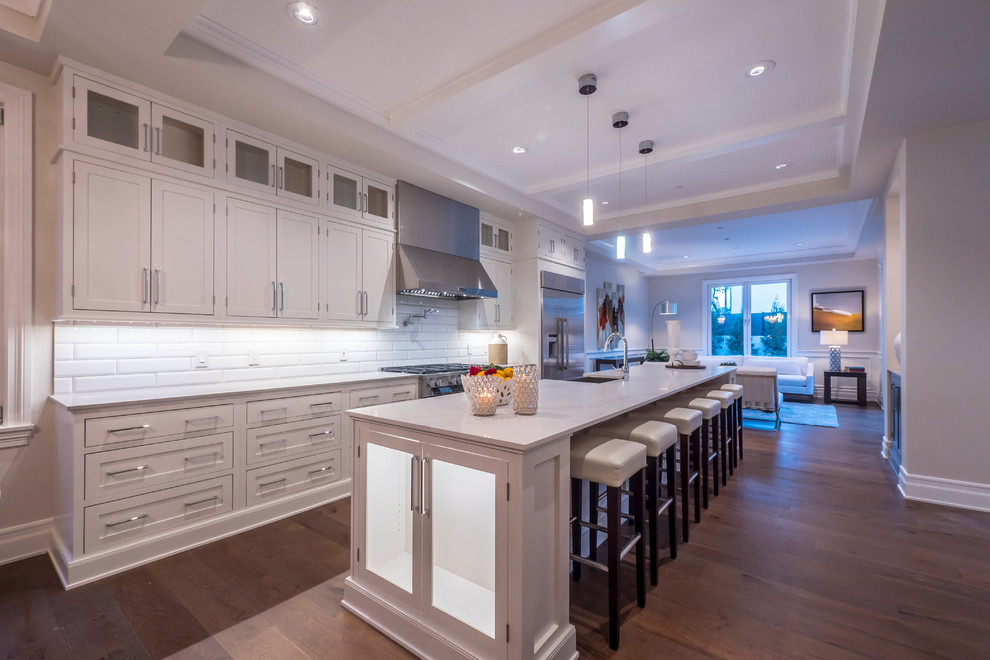 Ejemplo de cocina comedor lineal actual grande con salpicadero blanco, electrodomésticos de acero inoxidable, suelo de madera en tonos medios y una isla