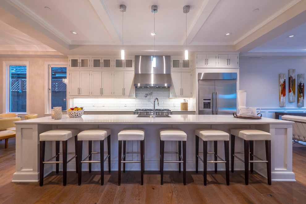 Foto på ett stort funkis linjärt kök och matrum, med vitt stänkskydd, rostfria vitvaror, mellanmörkt trägolv och en köksö