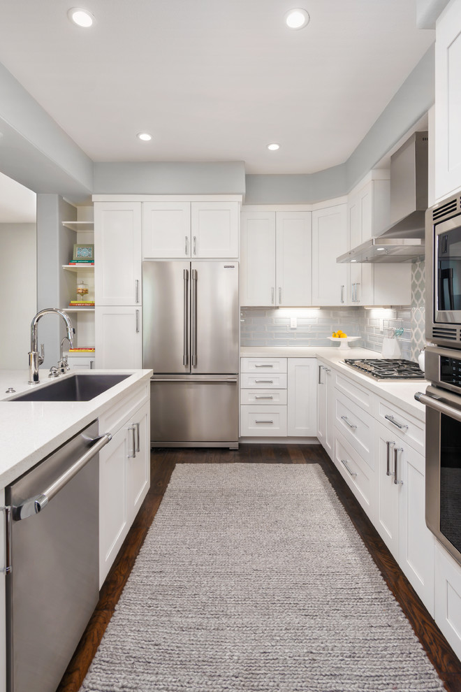This is an example of a small traditional l-shaped open plan kitchen in San Francisco with a submerged sink, shaker cabinets, white cabinets, engineered stone countertops, blue splashback, ceramic splashback, stainless steel appliances, dark hardwood flooring, an island and brown floors.