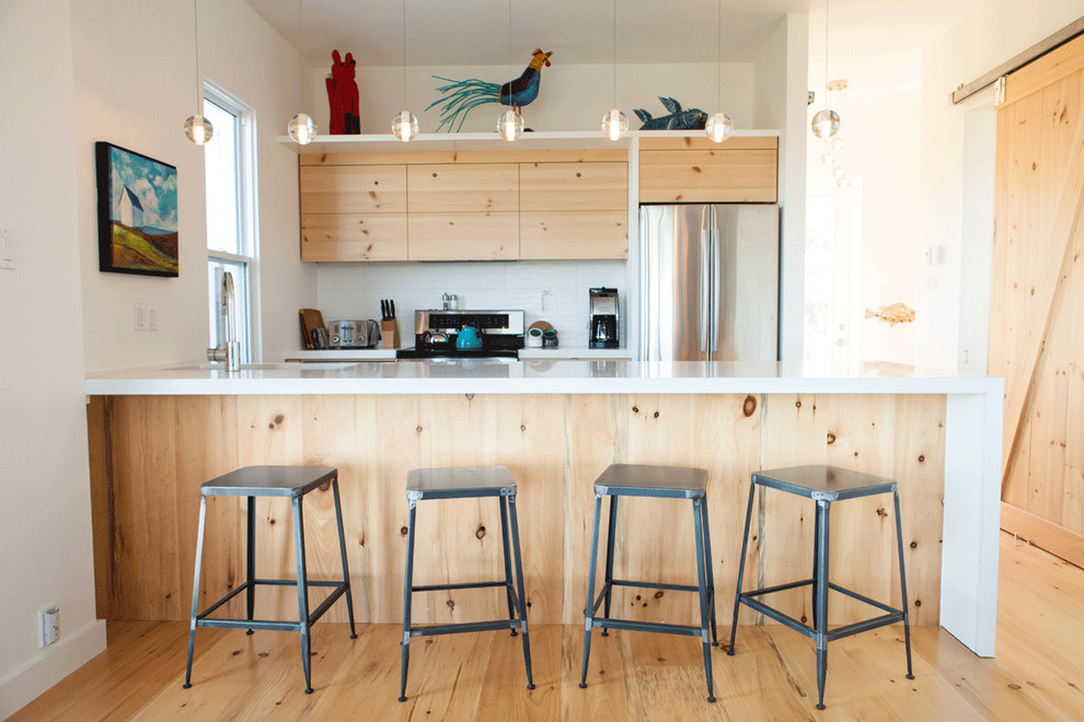 Diseño de cocina marinera con armarios con paneles lisos, puertas de armario de madera clara, electrodomésticos de acero inoxidable y salpicadero blanco