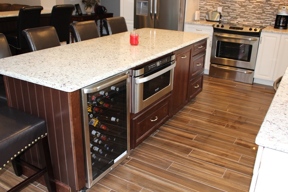 This is an example of a medium sized classic l-shaped kitchen/diner in Philadelphia with a submerged sink, raised-panel cabinets, dark wood cabinets, granite worktops, glass tiled splashback, stainless steel appliances, ceramic flooring and an island.