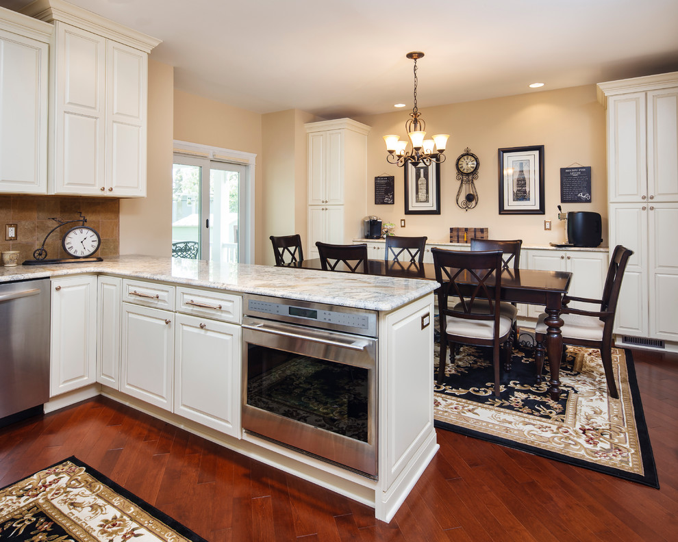 Klassisk inredning av ett stort kök, med en undermonterad diskho, luckor med upphöjd panel, vita skåp, granitbänkskiva, beige stänkskydd, stänkskydd i porslinskakel, rostfria vitvaror, mellanmörkt trägolv och en halv köksö