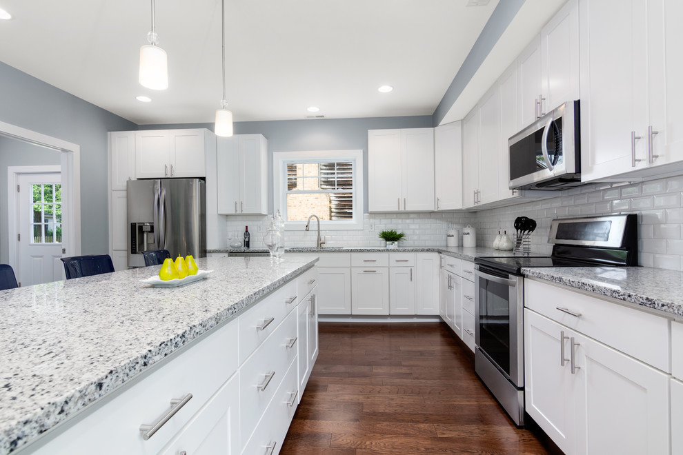 Klassisk inredning av ett stort grå grått kök, med en dubbel diskho, skåp i shakerstil, vita skåp, granitbänkskiva, vitt stänkskydd, stänkskydd i tunnelbanekakel, rostfria vitvaror, laminatgolv, en köksö och brunt golv