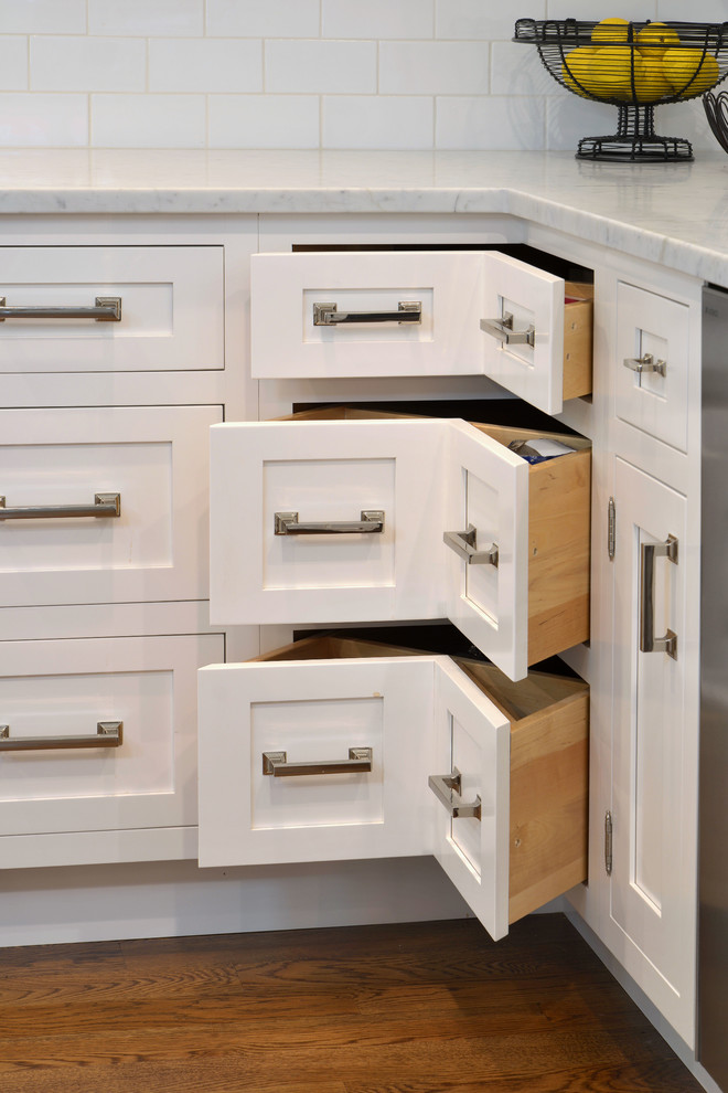 Elegant medium tone wood floor eat-in kitchen photo in New York with white cabinets and white backsplash