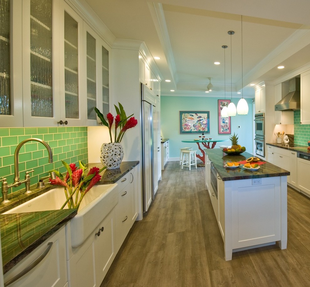 Exempel på ett exotiskt kök, med en rustik diskho, skåp i shakerstil, vita skåp, granitbänkskiva, grönt stänkskydd, stänkskydd i glaskakel, integrerade vitvaror, vinylgolv och en köksö