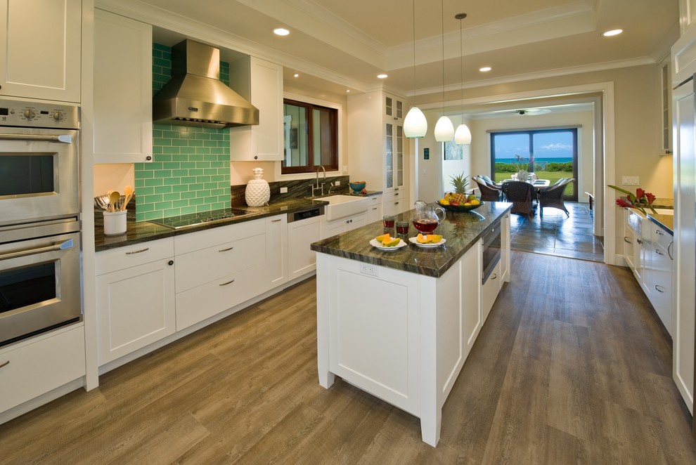 Inspiration for a tropical vinyl floor kitchen remodel in Hawaii with a farmhouse sink, shaker cabinets, white cabinets, granite countertops, green backsplash, glass tile backsplash, paneled appliances and an island