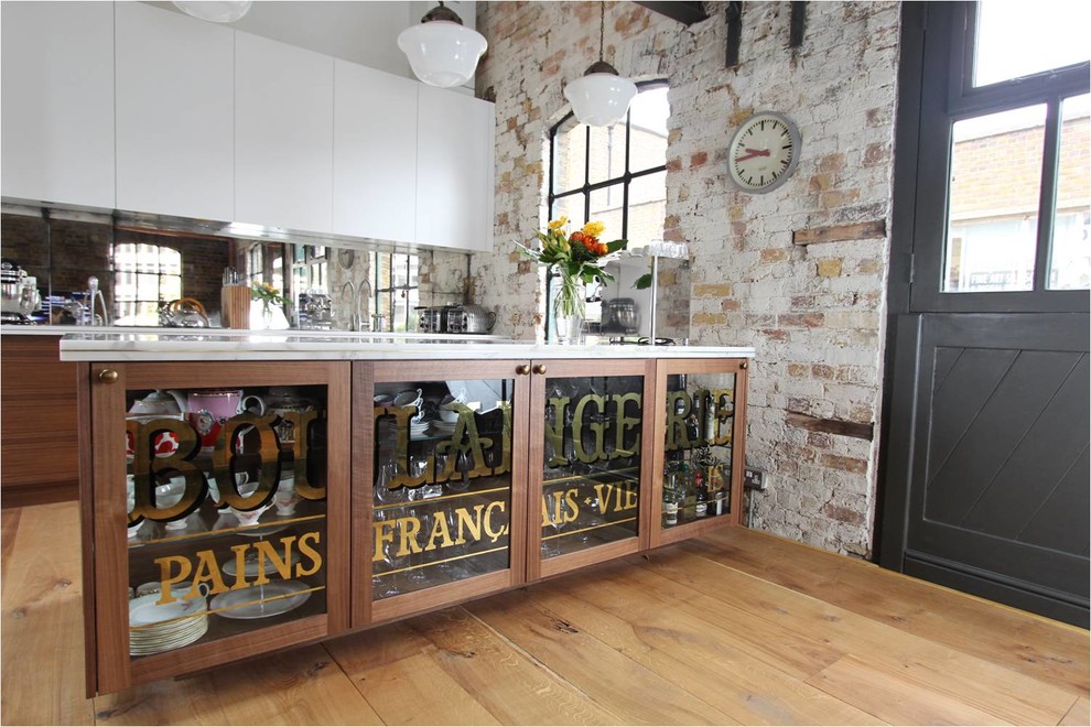 This is an example of a medium sized industrial open plan kitchen in London with marble worktops, glass sheet splashback and an island.