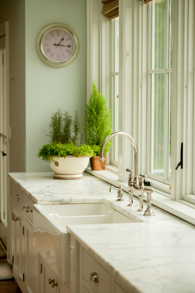 Large coastal u-shaped kitchen/diner in New York with a belfast sink, recessed-panel cabinets, white cabinets, marble worktops, white splashback, stainless steel appliances, light hardwood flooring and an island.