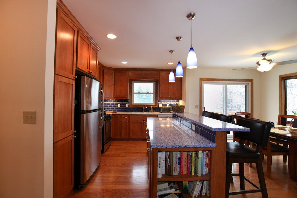 Trendy light wood floor eat-in kitchen photo in Minneapolis with medium tone wood cabinets, recycled glass countertops and blue backsplash