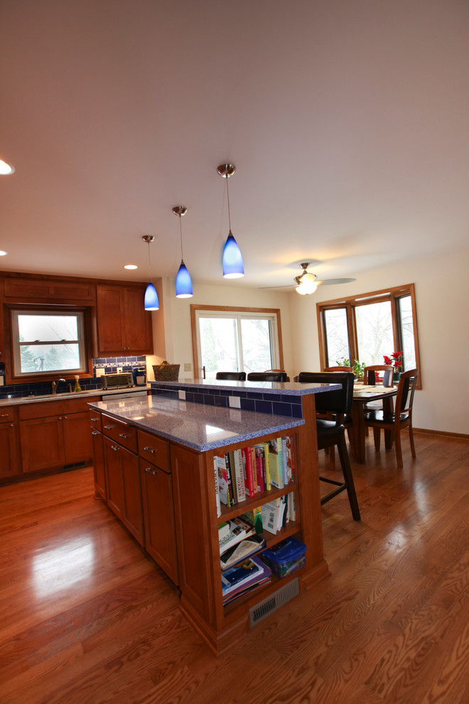 Modern inredning av ett kök och matrum, med skåp i mellenmörkt trä, bänkskiva i återvunnet glas, blått stänkskydd och ljust trägolv