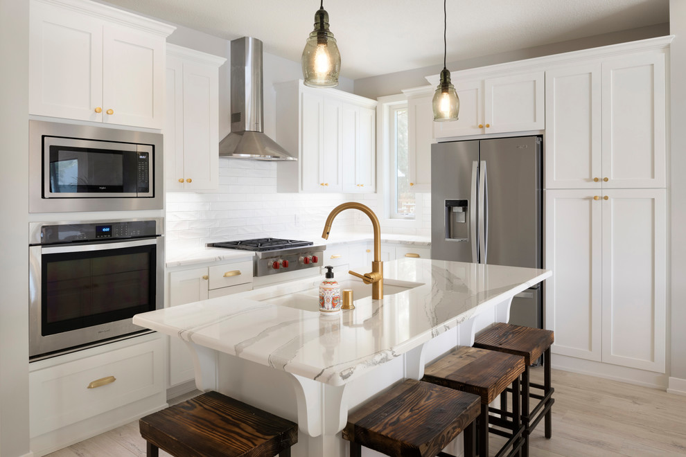 Photo of a medium sized classic l-shaped kitchen in Minneapolis with white cabinets, white splashback, stainless steel appliances, light hardwood flooring, an island, white worktops, a double-bowl sink, shaker cabinets, metro tiled splashback and beige floors.