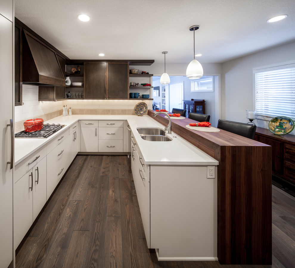 Modern inredning av ett mellanstort u-kök, med en dubbel diskho, släta luckor, träbänkskiva, vita skåp, integrerade vitvaror, stänkskydd i keramik, mörkt trägolv och en halv köksö