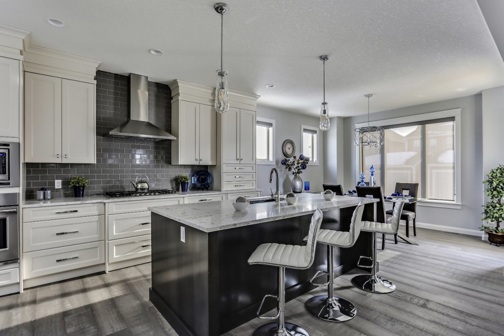 Photo of a medium sized classic l-shaped kitchen/diner in Calgary with a submerged sink, shaker cabinets, white cabinets, engineered stone countertops, grey splashback, metro tiled splashback, stainless steel appliances, painted wood flooring, an island, grey floors and white worktops.
