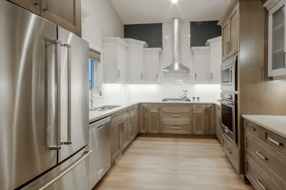 Modern inredning av ett mellanstort kök, med en undermonterad diskho, skåp i shakerstil, grå skåp, bänkskiva i kvarts, vitt stänkskydd, stänkskydd i tunnelbanekakel, rostfria vitvaror, laminatgolv och en halv köksö
