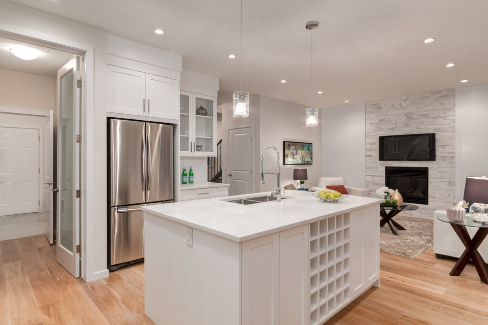 Example of a mid-sized trendy l-shaped medium tone wood floor open concept kitchen design in Calgary with a double-bowl sink, shaker cabinets, white cabinets, quartz countertops, white backsplash, ceramic backsplash, stainless steel appliances and an island