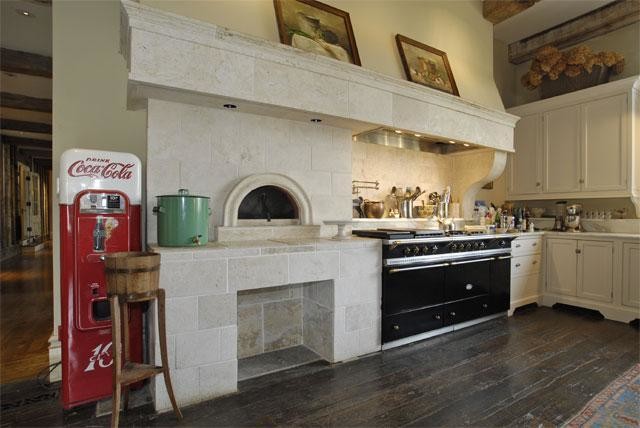 Lantlig inredning av ett kök, med en rustik diskho, luckor med profilerade fronter, vita skåp, marmorbänkskiva, vitt stänkskydd, stänkskydd i sten, svarta vitvaror och mellanmörkt trägolv