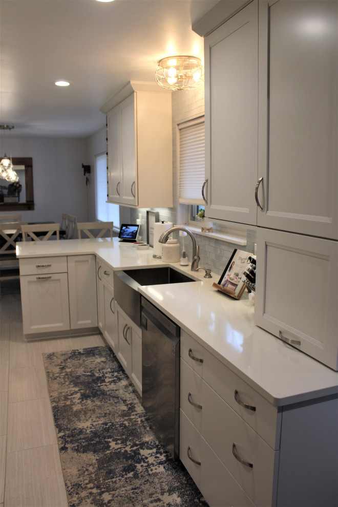 Foto på ett mellanstort vintage vit kök, med en rustik diskho, luckor med infälld panel, vita skåp, bänkskiva i kvarts, vitt stänkskydd, stänkskydd i glaskakel, rostfria vitvaror, klinkergolv i porslin, en halv köksö och grått golv