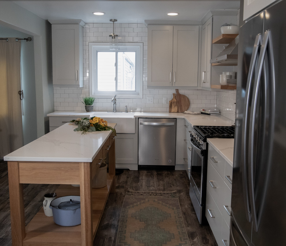 Inspiration for a mid-sized cottage l-shaped medium tone wood floor and gray floor enclosed kitchen remodel in Detroit with a farmhouse sink, recessed-panel cabinets, gray cabinets, quartz countertops, white backsplash, ceramic backsplash, stainless steel appliances, an island and white countertops