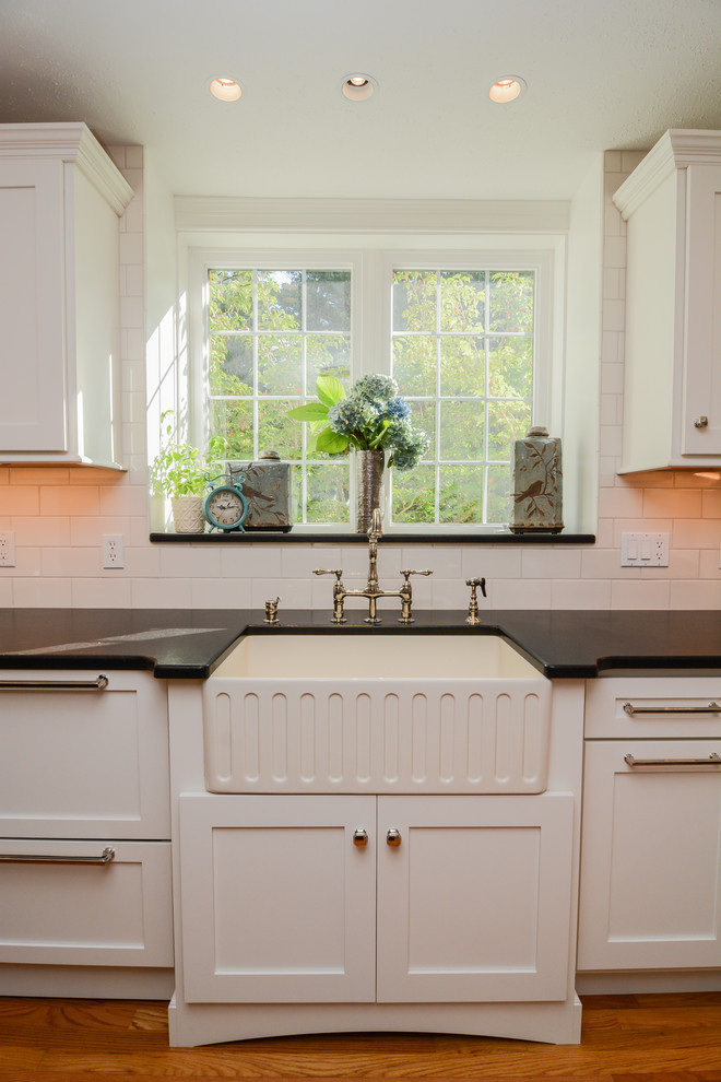 Klassisk inredning av ett stort kök, med en rustik diskho, skåp i shakerstil, vita skåp, granitbänkskiva, grått stänkskydd, stänkskydd i tunnelbanekakel, rostfria vitvaror, mellanmörkt trägolv och en köksö