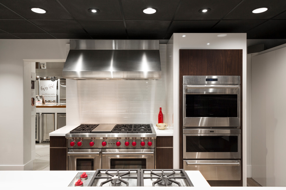 Photo of a modern kitchen/diner in San Francisco with flat-panel cabinets, dark wood cabinets, white splashback, metro tiled splashback, stainless steel appliances and an island.
