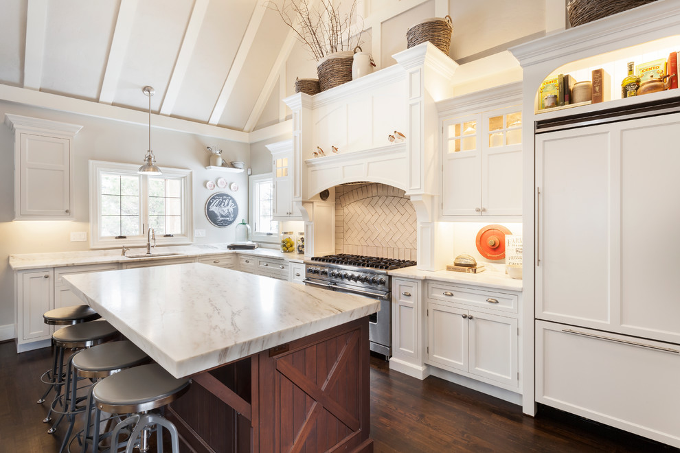 Klassisk inredning av ett mellanstort kök, med en nedsänkt diskho, luckor med profilerade fronter, vita skåp, marmorbänkskiva, grått stänkskydd, stänkskydd i tunnelbanekakel, rostfria vitvaror, mörkt trägolv och en köksö