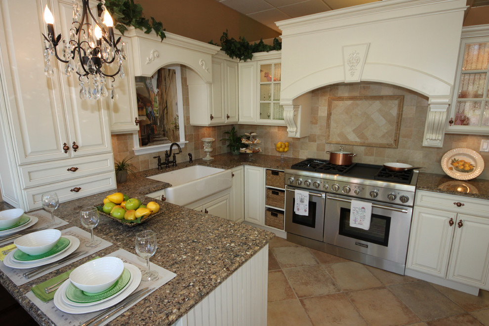 Mid-sized tuscan u-shaped travertine floor enclosed kitchen photo in New York with a farmhouse sink, raised-panel cabinets, white cabinets, granite countertops, beige backsplash, stone tile backsplash, stainless steel appliances and a peninsula