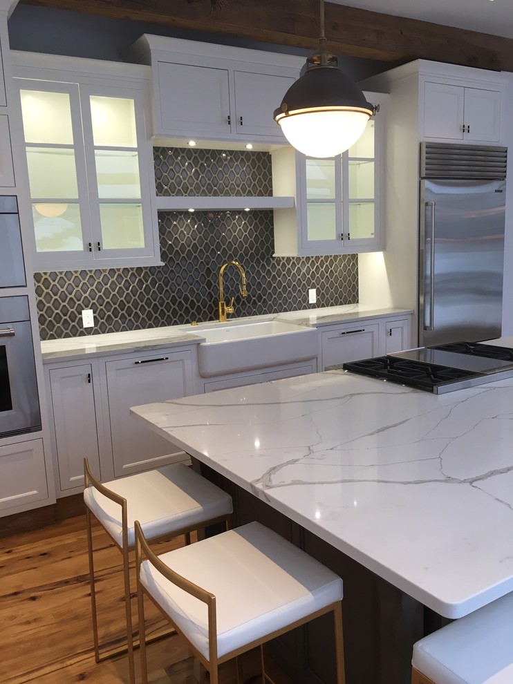 Photo of an expansive classic single-wall kitchen/diner in Bridgeport with a belfast sink, shaker cabinets, white cabinets, engineered stone countertops, brown splashback, ceramic splashback, stainless steel appliances, light hardwood flooring, an island, yellow floors and white worktops.