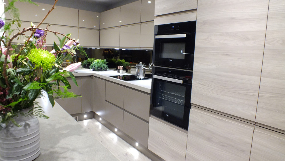 Immagine di una cucina contemporanea di medie dimensioni con elettrodomestici neri, pavimento in laminato, ante lisce, top in laminato, paraspruzzi a effetto metallico, paraspruzzi a specchio e top beige
