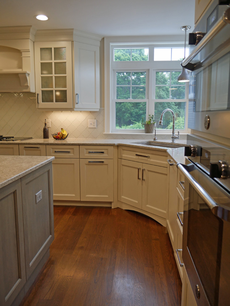 Idéer för stora vintage kök, med en undermonterad diskho, luckor med infälld panel, vita skåp, bänkskiva i kvarts, vitt stänkskydd, stänkskydd i glaskakel, rostfria vitvaror, mellanmörkt trägolv, en köksö och brunt golv
