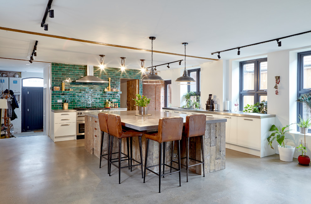 This is an example of an urban l-shaped kitchen in Other with flat-panel cabinets, white cabinets, stainless steel worktops, green splashback, metro tiled splashback, concrete flooring, an island, grey floors and grey worktops.