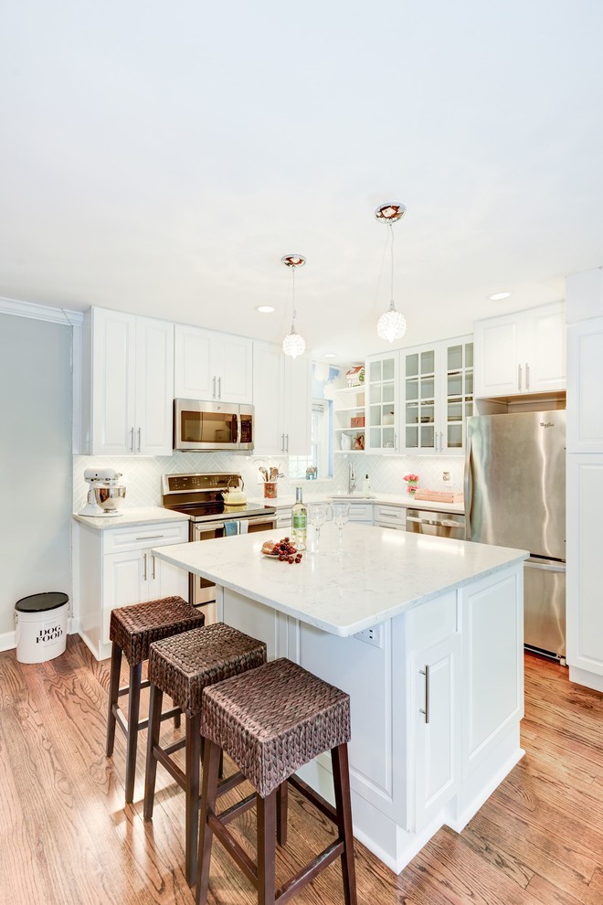 Photo of a medium sized contemporary l-shaped kitchen/diner in DC Metro with a submerged sink, shaker cabinets, white cabinets, engineered stone countertops, white splashback, porcelain splashback, stainless steel appliances, medium hardwood flooring and an island.