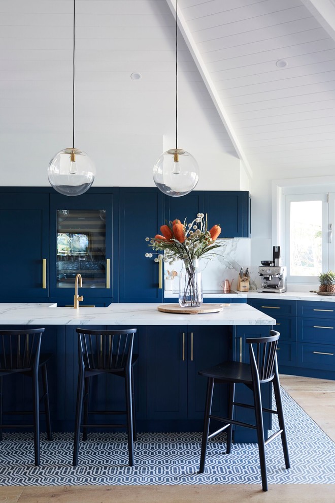 Exemple d'une cuisine ouverte parallèle et encastrable avec un évier de ferme, un placard à porte shaker, des portes de placard bleues, une crédence blanche, parquet clair, îlot et un plan de travail blanc.